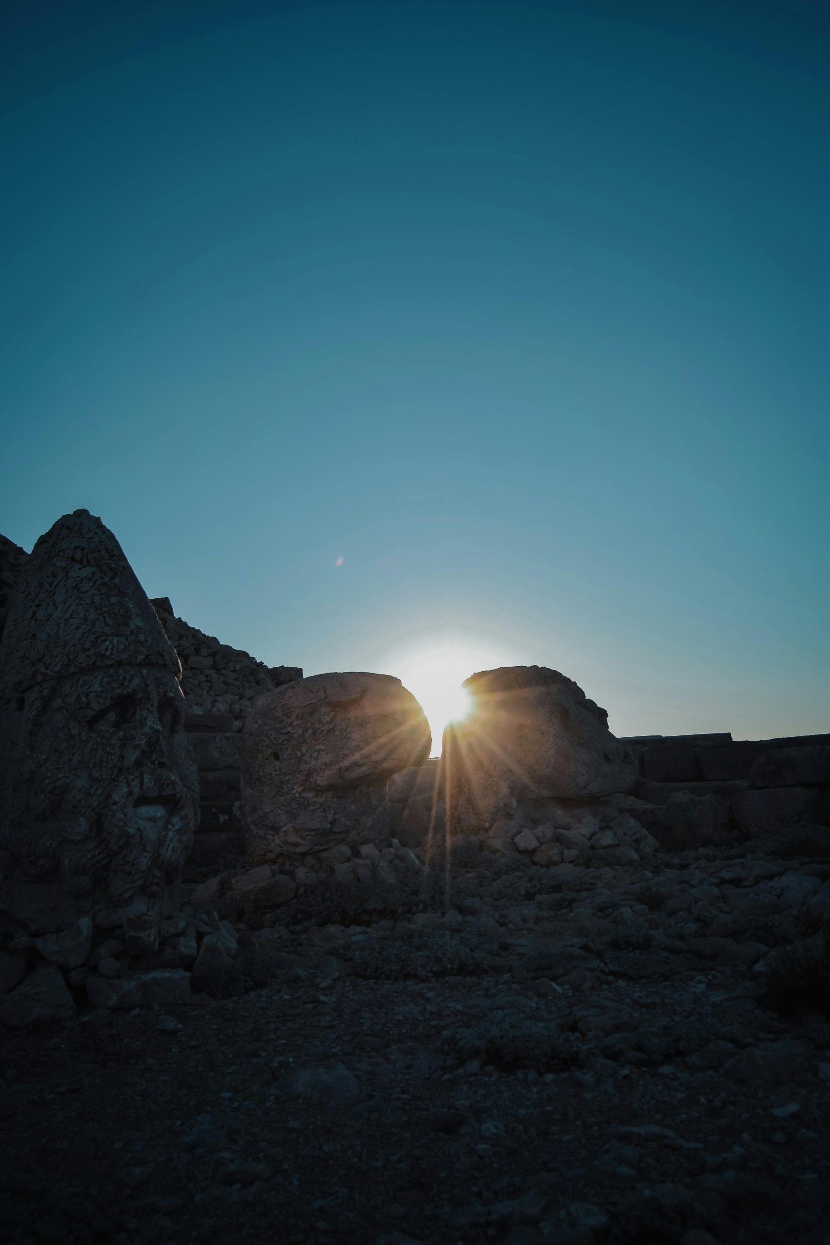 The sun rises between two rocks, casting a warm glow on the surrounding area.